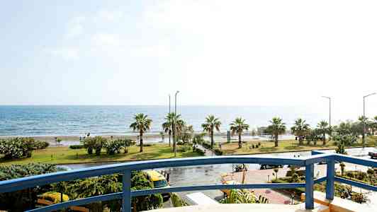 Utsikt från en balkong mot en kustlinje med palmer och hav. (AI-genererad text)