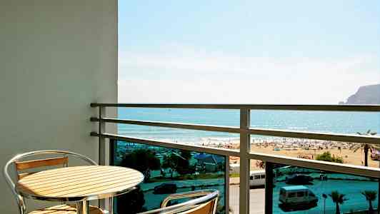 Balkong med ett bord och två stolar, utsikt mot stranden och havet. (AI-genererad text)