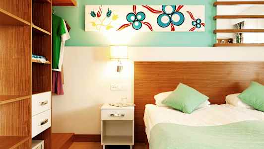 Ett sovrum med en säng, två gröna kuddar, en träbeklädd garderob och en nattduksbord med en lampa. (AI-genererad text)