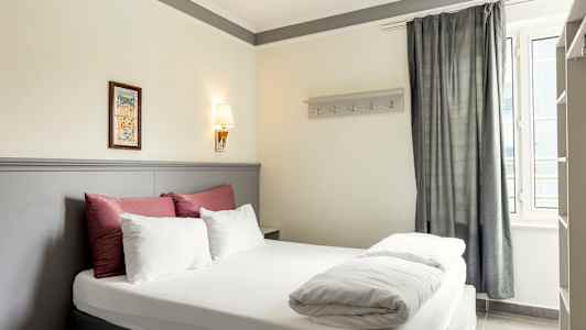 Bild på ett hotellrum med en dubbelsäng, dekorerad med sängkläder i vitt och rött samt en ljusgrå sänggavel. (AI-genererad text)