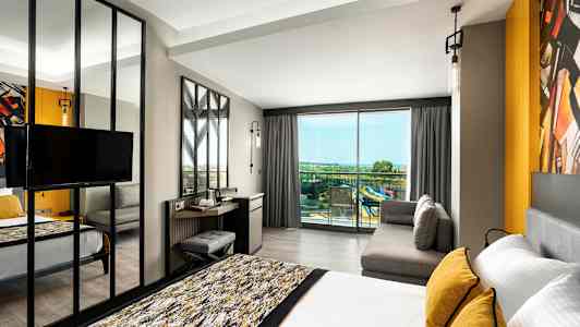 Modernt hotellrum med säng, soffa och utsikt mot balkong med panoramavy. (AI-genererad text)