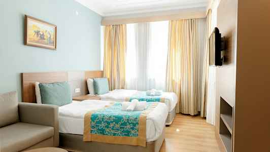 Hotellrum med två enkelsängar, en soffa och en TV på väggen. (AI-genererad text)