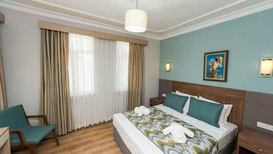 Hotellrum med dubbelsäng, sänglampor, en målning på väggen och en stol vid fönstret. (AI-genererad text)