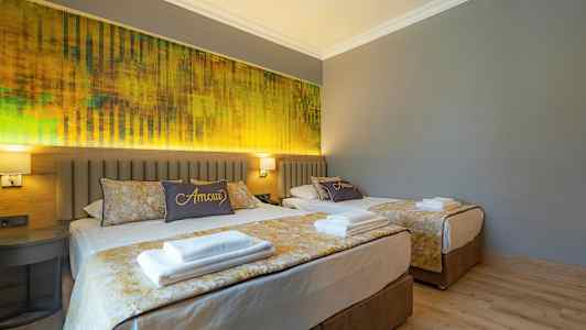 Två sängar i ett hotellrum med grå väggar och gul inredning. (AI-genererad text)