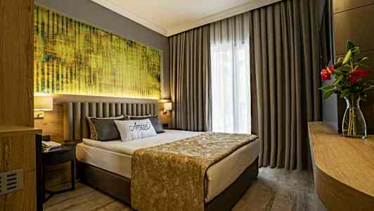 Ett hotellrum med en dubbelsäng, grå gardiner och en tavla ovanför sängen. (AI-genererad text)