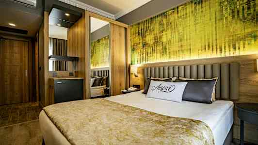 Ett modernt hotellrum med en dubbelsäng, dekorativ kudde och färgglad väggkonst. (AI-genererad text)