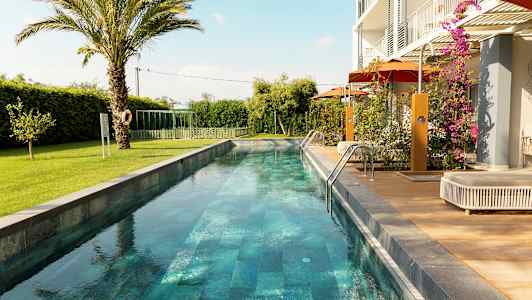 En lång smal pool omgiven av grönska och ett modernt boende. (AI-genererad text)