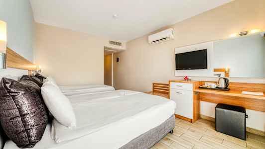 Ett hotellrum med två sängar, ett skrivbord, en spegel och en väggmonterad TV. (AI-genererad text)