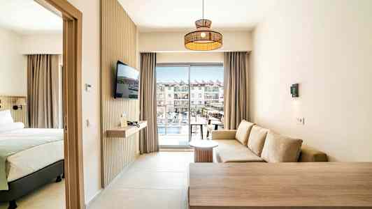 Ett hotellrum med en sittgrupp, en säng och en TV, samt en balkong med utsikt över poolområdet. (AI-genererad text)