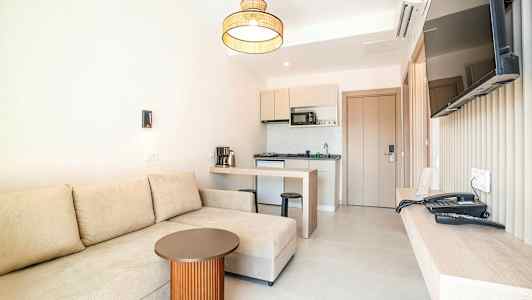 Ett hotellrum med en beige soffa, ett litet bord, ett kök och en väggmonterad TV. (AI-genererad text)