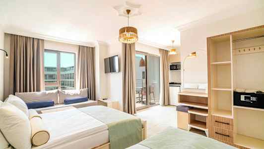 Bild på ett hotellrum med moderna möbler, två sängar, en soffa, ett TV och en balkong med ljusa gardiner. (AI-genererad text)