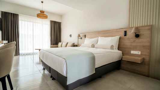 En hotellrum med en dubbelsäng, soffa och stora fönster med ljusa gardiner. (AI-genererad text)