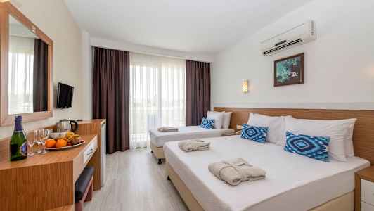 Hotellrum med två enkelsängar bäddade med vita lakan och blå kuddar, samt ett bord med frukt och drycker. (AI-genererad text)