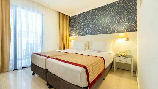 Hotellrum med två enkelsängar, dekorativt tapetmönster och fönster med gardiner. (AI-genererad text)