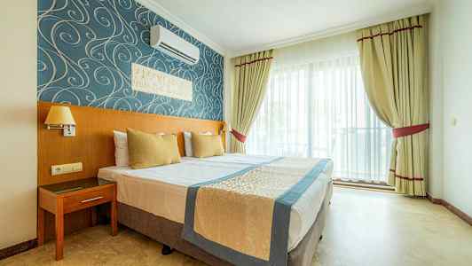 Hotellrum med dubbelsäng, blå och guldfärgad inredning samt fönster med ljusa gardiner. (AI-genererad text)