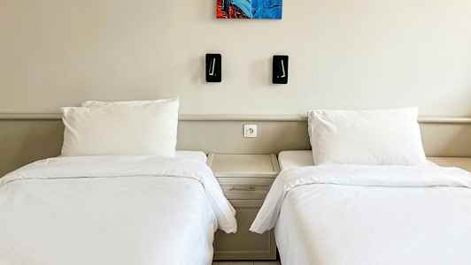 Två enkelsängar med vita sängkläder och en gemensam sänghylla mellan dem. (AI-genererad text)