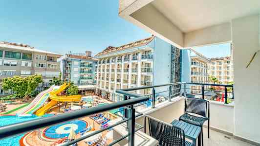 Balkong med utsikt över hotellbyggnader och en pool med vattenrutschbana. (AI-genererad text)