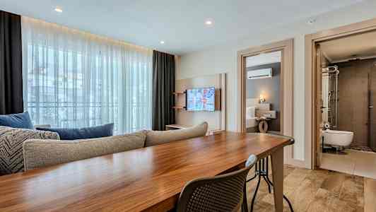 Interiör av ett modernt hotellrum med bord, soffa, TV och angränsande sovrum och badrum. (AI-genererad text)