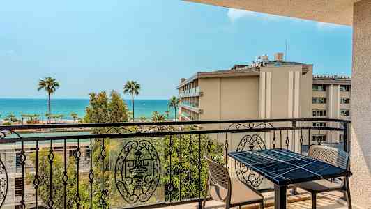 Utsikt över en balkong med bord och stolar, samt hav och palmer i bakgrunden. (AI-genererad text)