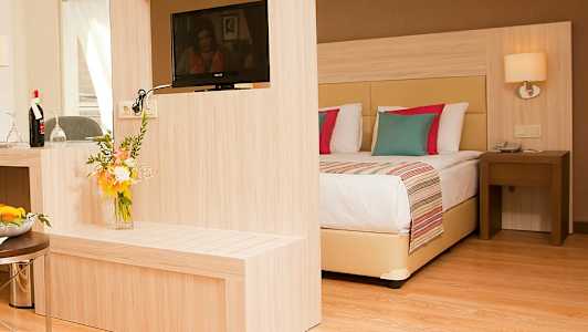 Ett hotellrum med en modern inredning, inklusive en dubbelsäng, en TV på en träpanel och en blombukett. (AI-genererad text)