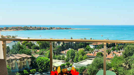 Utsikt från en balkong över havet och bebyggelse med träd och byggnader. (AI-genererad text)