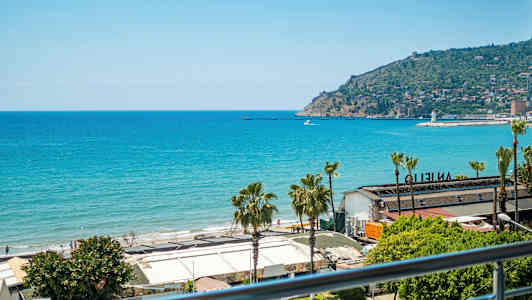 Utsikt över havet och en strand med byggnader i förgrunden. En udde med bebyggelse är synlig i bakgrunden. (AI-genererad text)