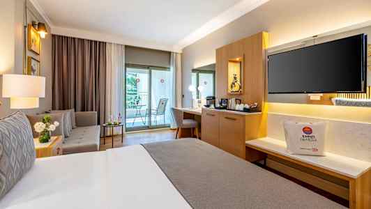 Ett välmöblerat hotellrum med en dubbelsäng, sittgrupp, skrivbord och en balkong. (AI-genererad text)