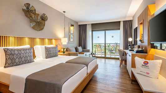 Hotellrum med två enkelsängar, dekorativ belysning och utsikt mot en balkong med möbler. (AI-genererad text)