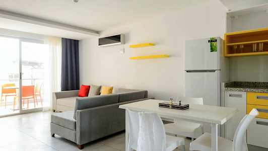 Ett vardagsrum med grå soffa, färgade kuddar, matbord med stolar, och en öppen balkong. (AI-genererad text)