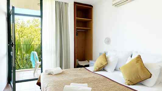 Ett hotellrum med en bäddad säng, öppet skåp och en balkongdörr som leder ut till en uteplats. (AI-genererad text)