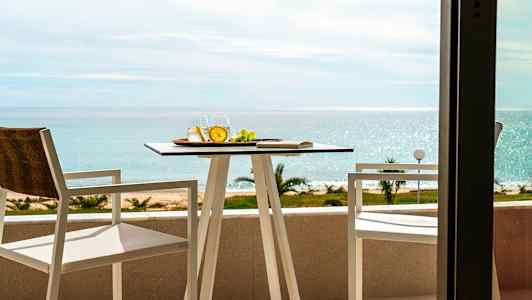 Två stolar och ett bord på en balkong med utsikt över havet. (AI-genererad text)