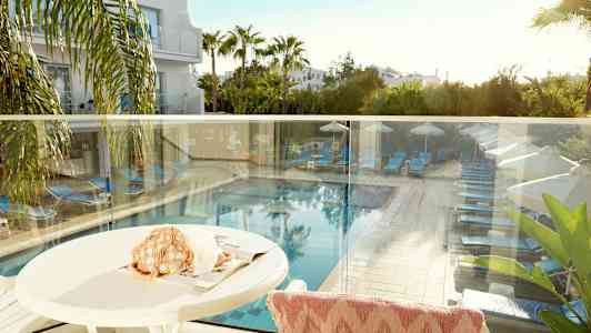 Utsikt från en terrass som visar en pool med solsängar och parasoller omgiven av grönska. (AI-genererad text)