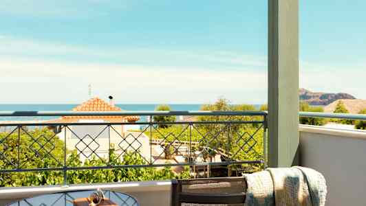 Utsikt från en balkong med ett glasbord och stol. Havet och hus syns i bakgrunden. (AI-genererad text)