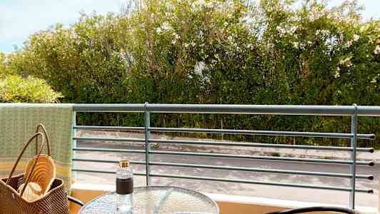 Utsikt från en balkong med ett glasbord, stolar och grönskande växtlighet i bakgrunden. (AI-genererad text)