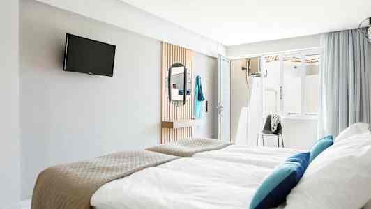 Hotellrum med sängar, TV på väggen, och en spegel. (AI-genererad text)