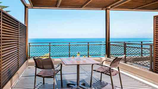 Terrass med havsutsikt, bord och två stolar under träpergola. (AI-genererad text)