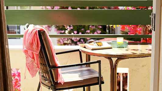 En stol med ett rosa plagg, ett bord med solglasögon, en bok och ett ljus står på en terrass. (AI-genererad text)