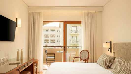 Modernt hotellrum med dubbelsäng, skrivbord, TV och balkong med utsikt. (AI-genererad text)