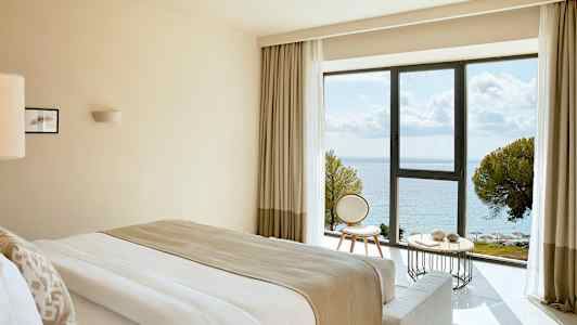 Hotellrum med havsutsikt genom ett stort fönster. (AI-genererad text)