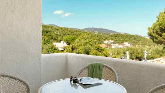 Utsikt från en balkong med ett bord, solglasögon och tidning, samt grönskande omgivningar. (AI-genererad text)