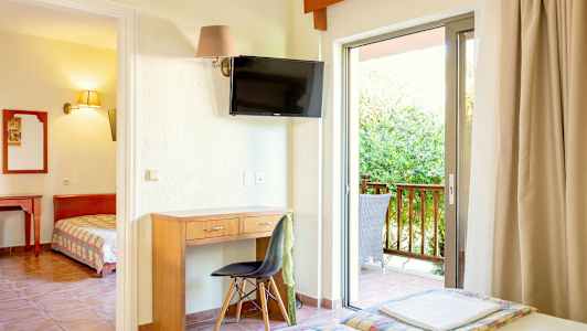 Ett hotellrum med skrivbord, stol, TV och balkong med utomhusstolar. (AI-genererad text)