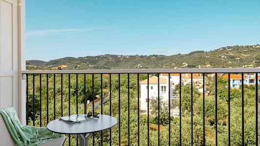 Utsikt från en balkong med bord och stol över ett lummigt landskap med hus och berg. (AI-genererad text)