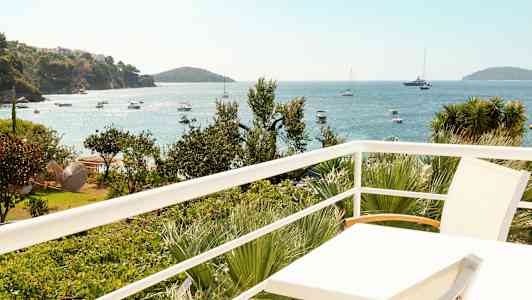 Utsikt från en balkong över havet med båtar och grönska. (AI-genererad text)