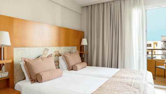 Två bäddar i ett hotellrum med ljusa textiler och trädetaljer. (AI-genererad text)