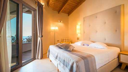 Ett hotellrum med en säng, en strukturerad vit sänggavel och en taklampa. Glasdörren leder till en balkong. (AI-genererad text)