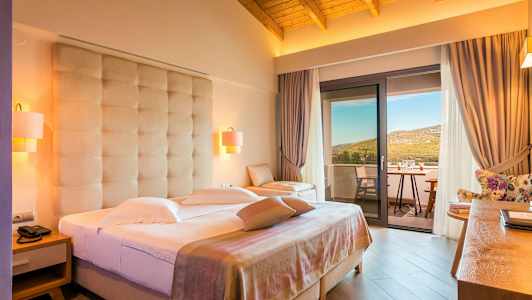 Ett hotellrum med dubbelsäng, sittmöbler och en balkong med utsikt över naturen. (AI-genererad text)