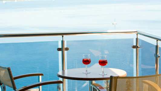 Två glas med röd dryck på ett bord på en balkong med utsikt över havet. (AI-genererad text)