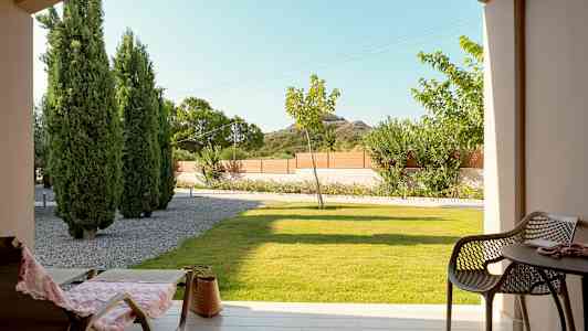 Utsikt från en terrass med stolar och bord, gräsmatta och träd i bakgrunden. (AI-genererad text)