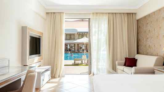 Hotellrum med balkong, säng, soffa och utsikt mot en pool. (AI-genererad text)