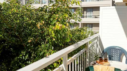 Bild på en balkong med bord, stol och grönska i förgrunden. (AI-genererad text)